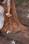 Brown saree with white floral patterns on a stone surface, featuring the brand 'Shivangi'.