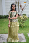 Young girl in a green and beige traditional outfit standing outdoors.