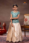 Young girl in a blue top and beige skirt standing in a room with decorative elements.