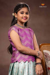 Young girl in a purple top and light blue skirt sitting on a chair with a brown background.