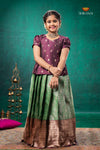 Woman in a traditional outfit with a green and brown skirt against a teal background