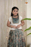 Young girl in traditional outfit standing against a light curtain background