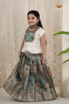 Young girl wearing a traditional outfit with a floral top and skirt against a decorative curtain background.